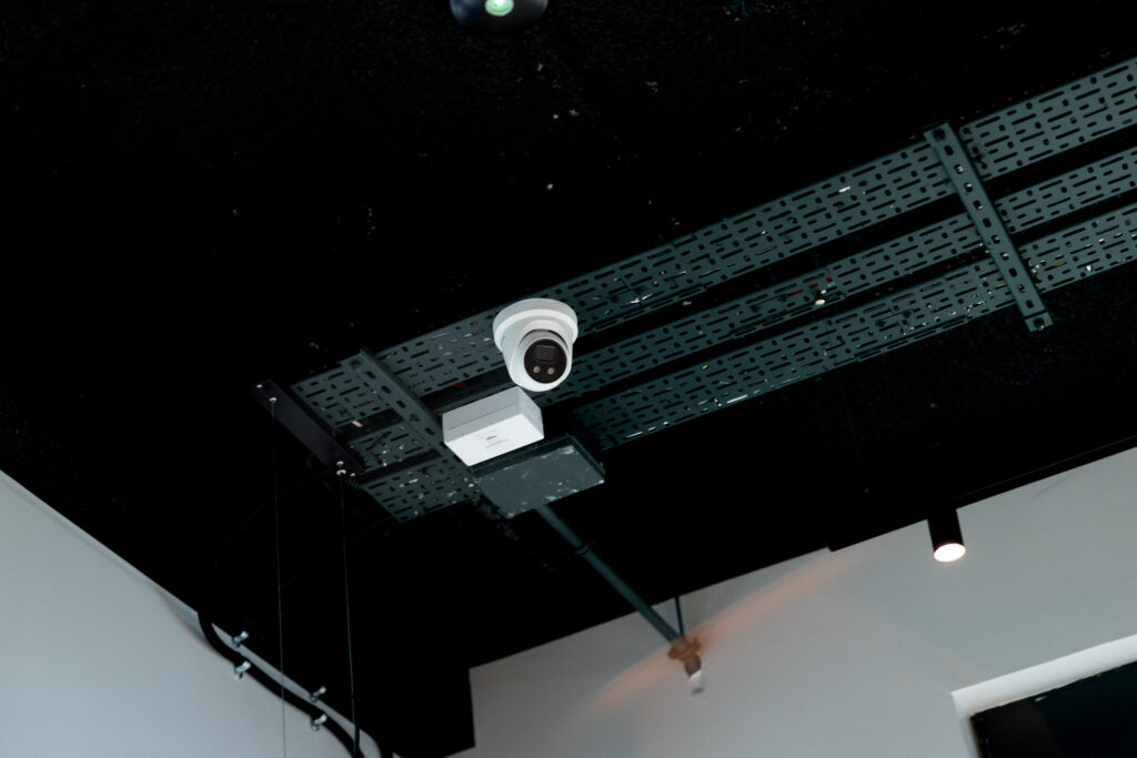 A white dome CCTV camera mounted on cable tray beneath the black ceiling of a commercial interior